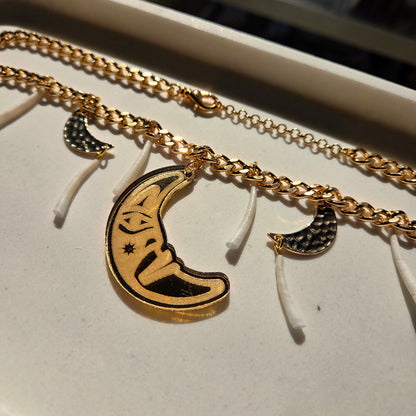 Gold chain necklace with moon pendant and dentalium on a white surface from Copper Canoe Woman.
