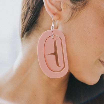 Close up of model wearing large ovoid earring with trigon cutout in antique peach color acrylic.