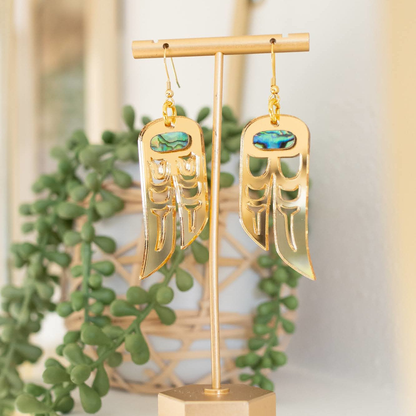 Gold mirror acrylic "Love Birds" earrings hang from a display stand from Copper Canoe Woman.