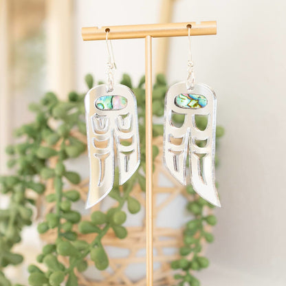 A pair of silver mirror acrylic "Love Birds" earrings from Copper Canoe Woman hang from a display stand.