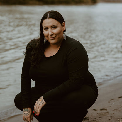 A model kneels by water while wearing silver mirror "Love Birds" earrings from Copper Canoe Woman.
