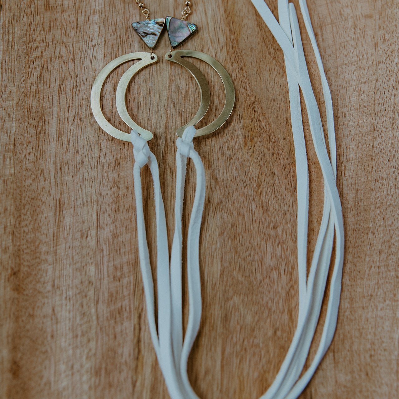 Brass crescent moon earrings topped with triangle abalone beads and white fringe hide that hangs from bottom of moon. Designed by Copper Canoe Woman