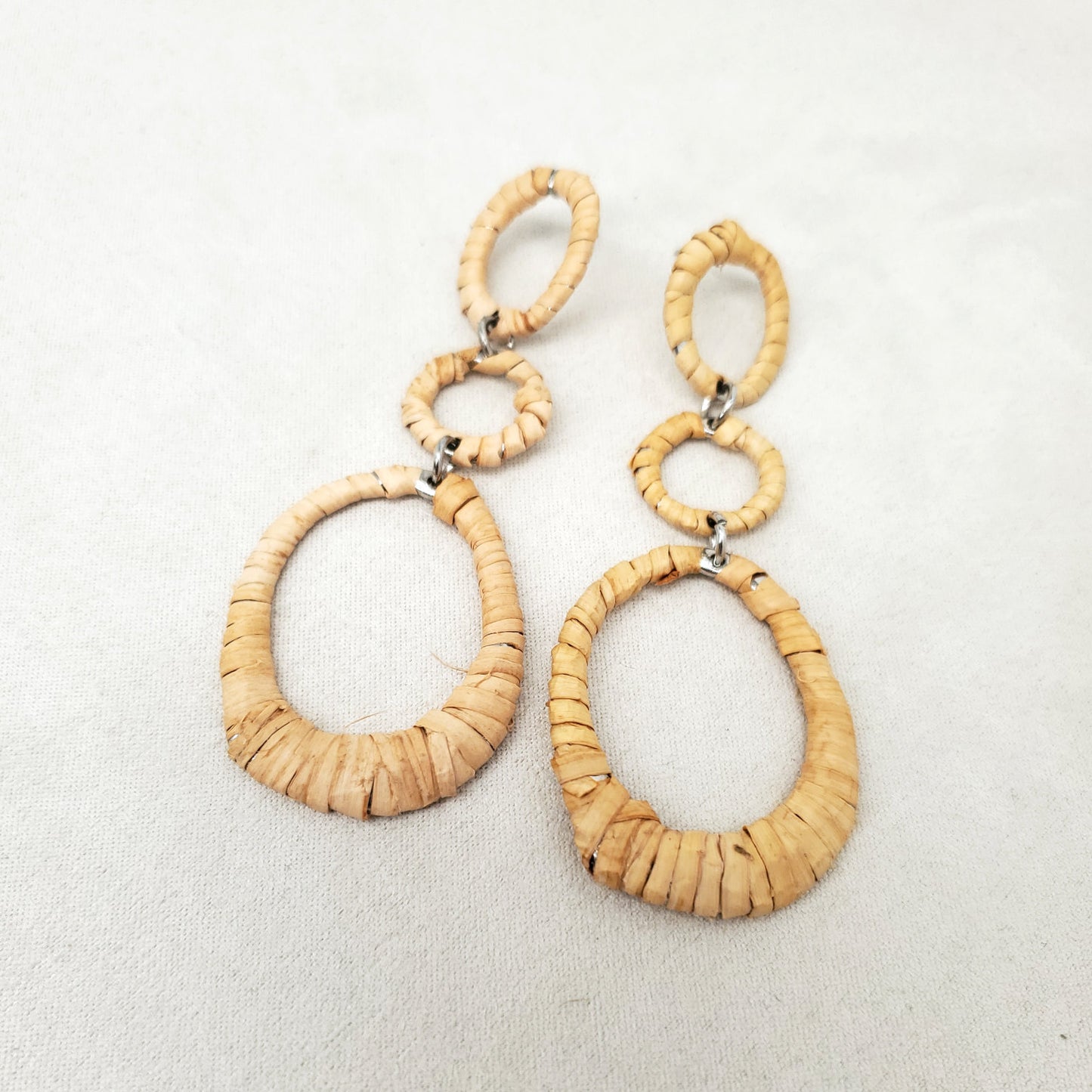 Three-tier woven cedar oval dangle earrings rest on a light gray background
