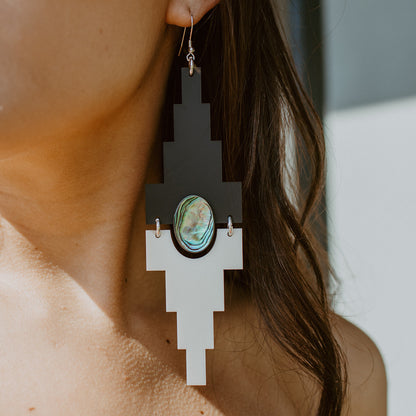 A closeup of Copper Canoe Woman "Mesa" earrings in jet black and cream acrylic worn by a model.