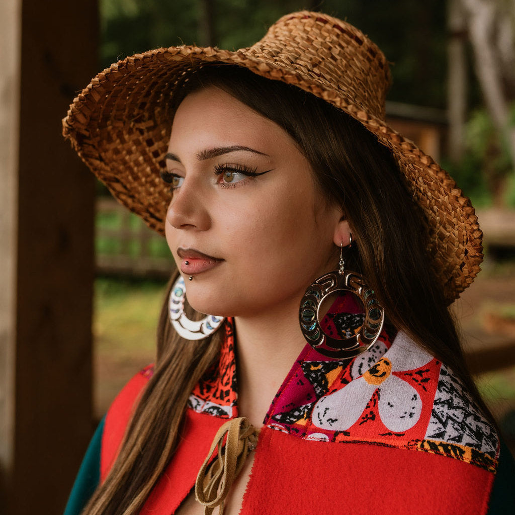 A model in a cedar hat wearing silver mirror acrylic Nala Hoop earrings from Copper Canoe Woman.