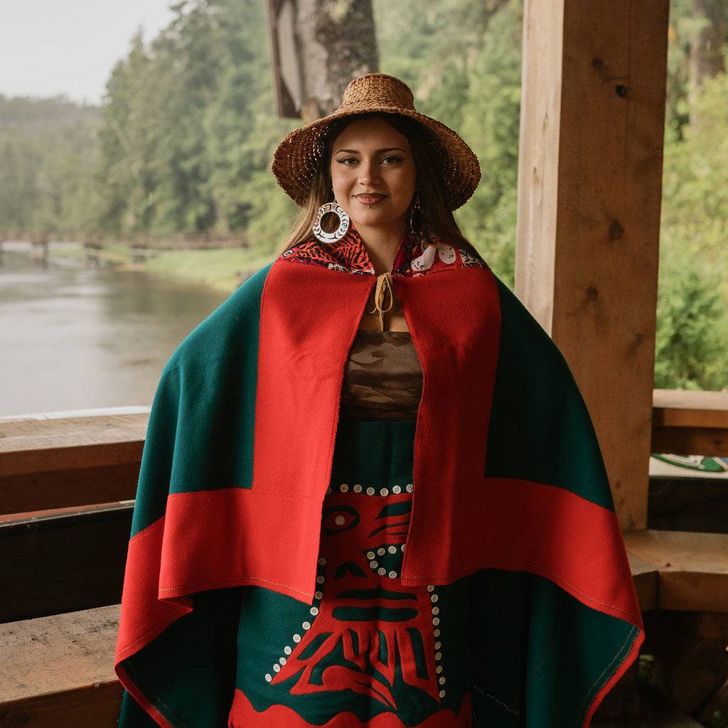 Woman wearing traditional Indigenous regalia stands in a wooden structure wearing silver mirror acrylic Nala Hoop earrings from Copper Canoe Woman.