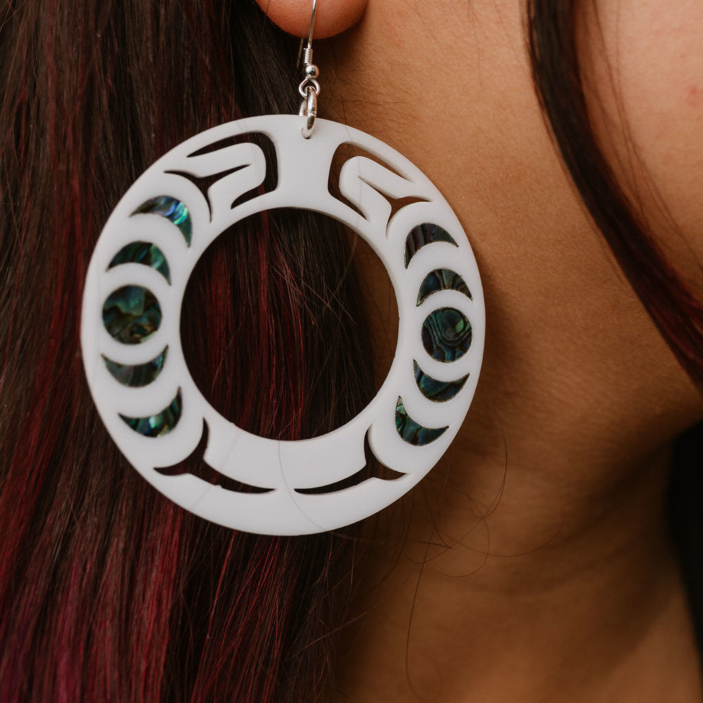 Close-up of a person wearing a white acrylic Nala Hoop earring with abalone inlay patterns from Copper Canoe Woman.