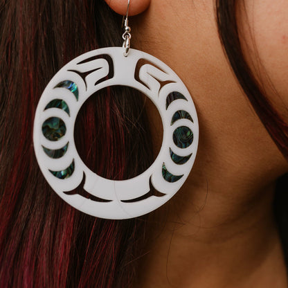 Close-up of a person wearing a white acrylic Nala Hoop earring with abalone inlay patterns from Copper Canoe Woman.