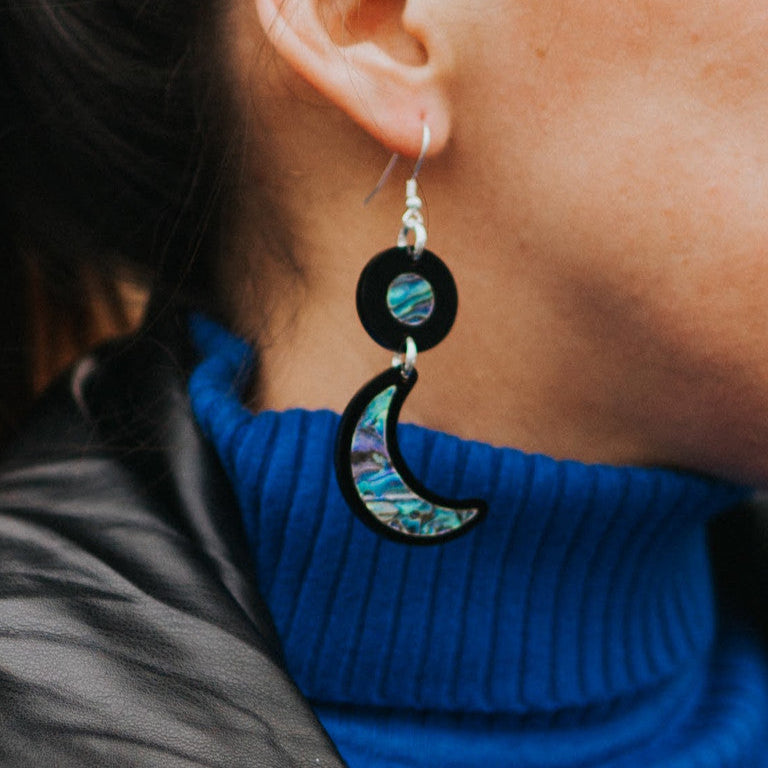 A closeup of a model wearing black acrylic "Nuci" crescent moon earrings from Copper Canoe Woman.