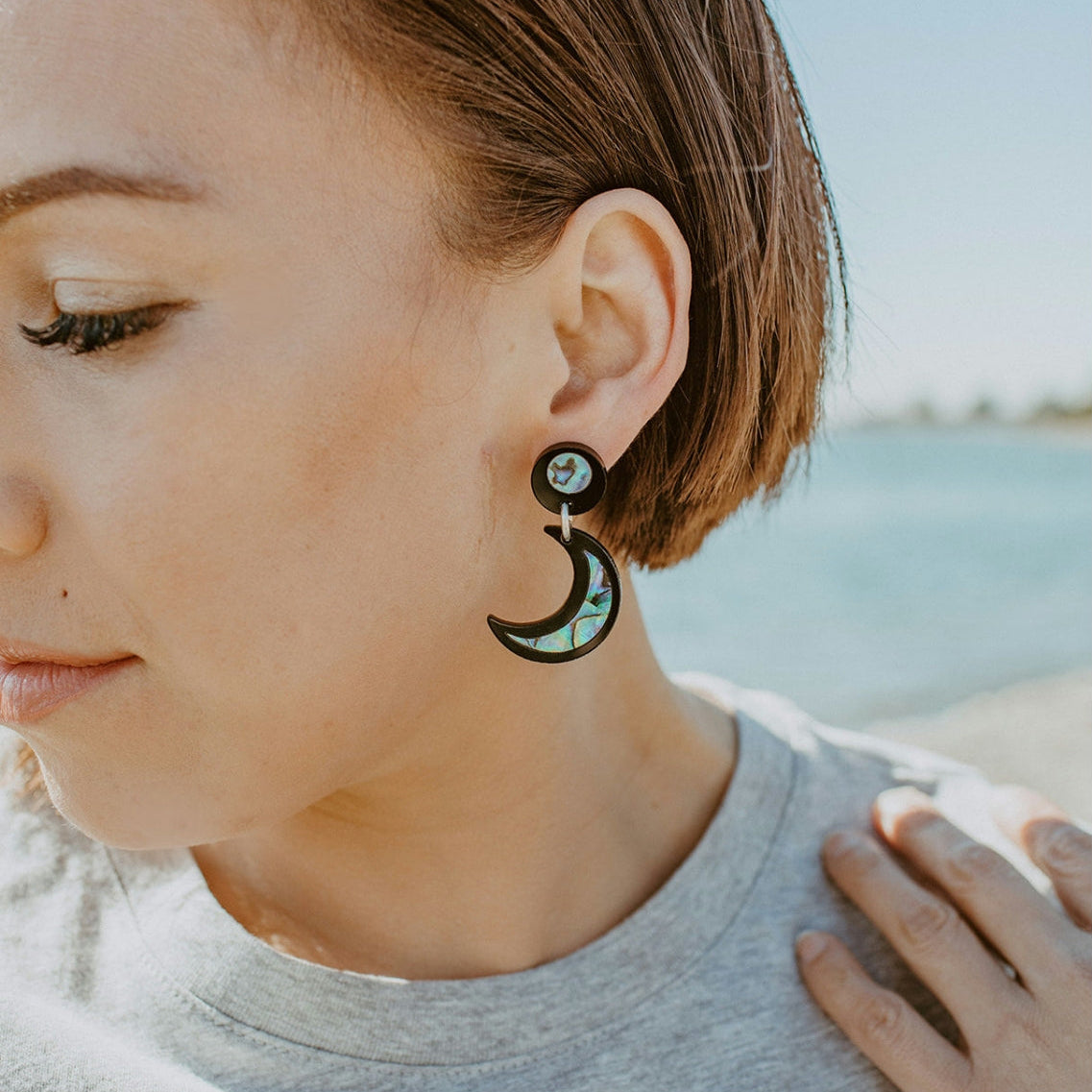 A model in closeup wearing black acrylic "Nuci" crescent moon earrings from Copper Canoe Woman.