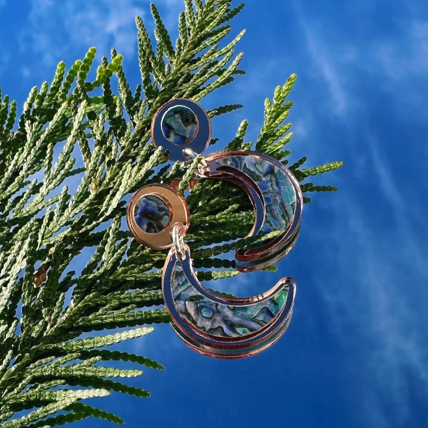A pair of "Nuci" crescent moon post earrings in rose gold mirror acrylic from Copper Canoe Woman.