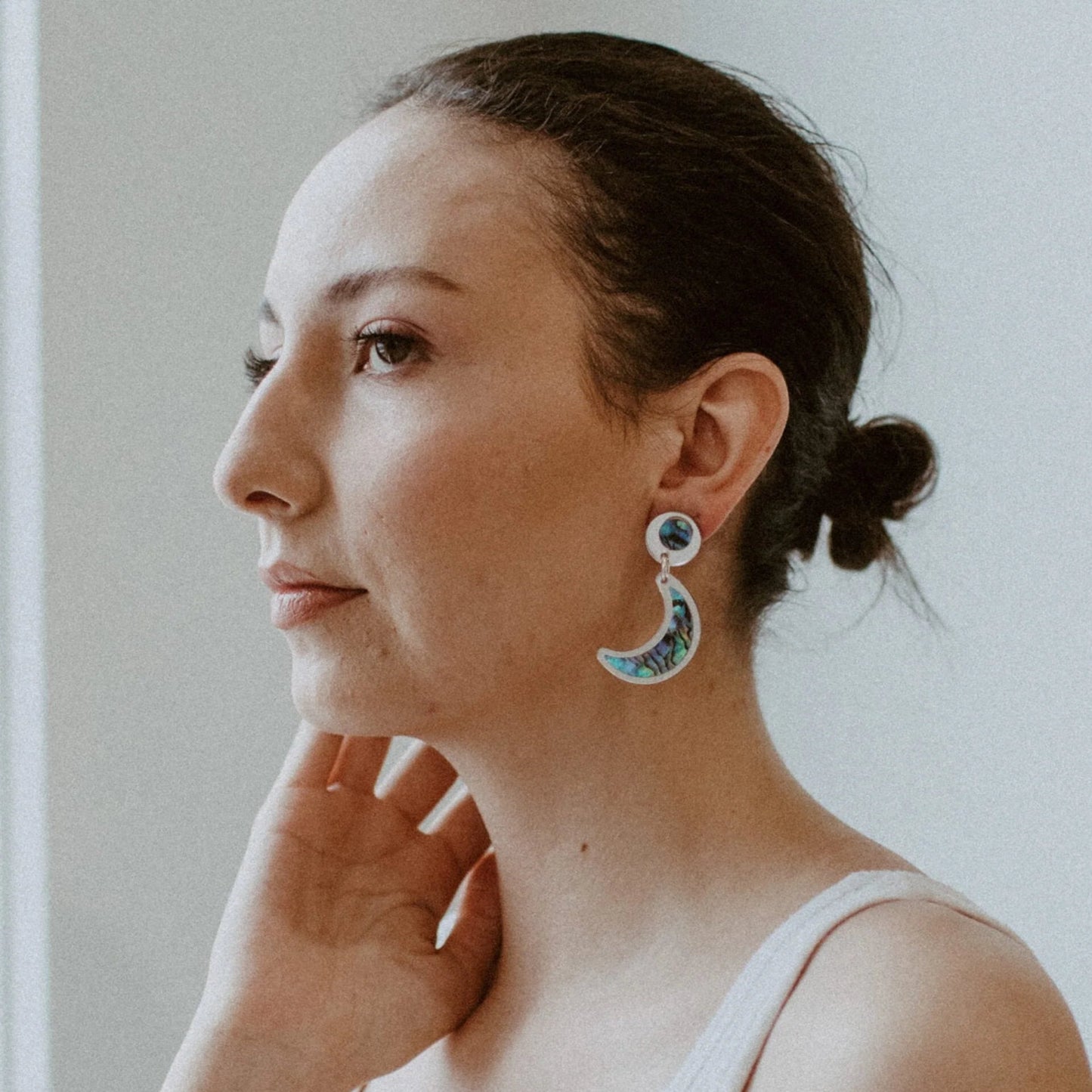A model wearing the post version of the "Nuci" crescent moon earring in silver mirror acrylic from Copper Canoe Woman.