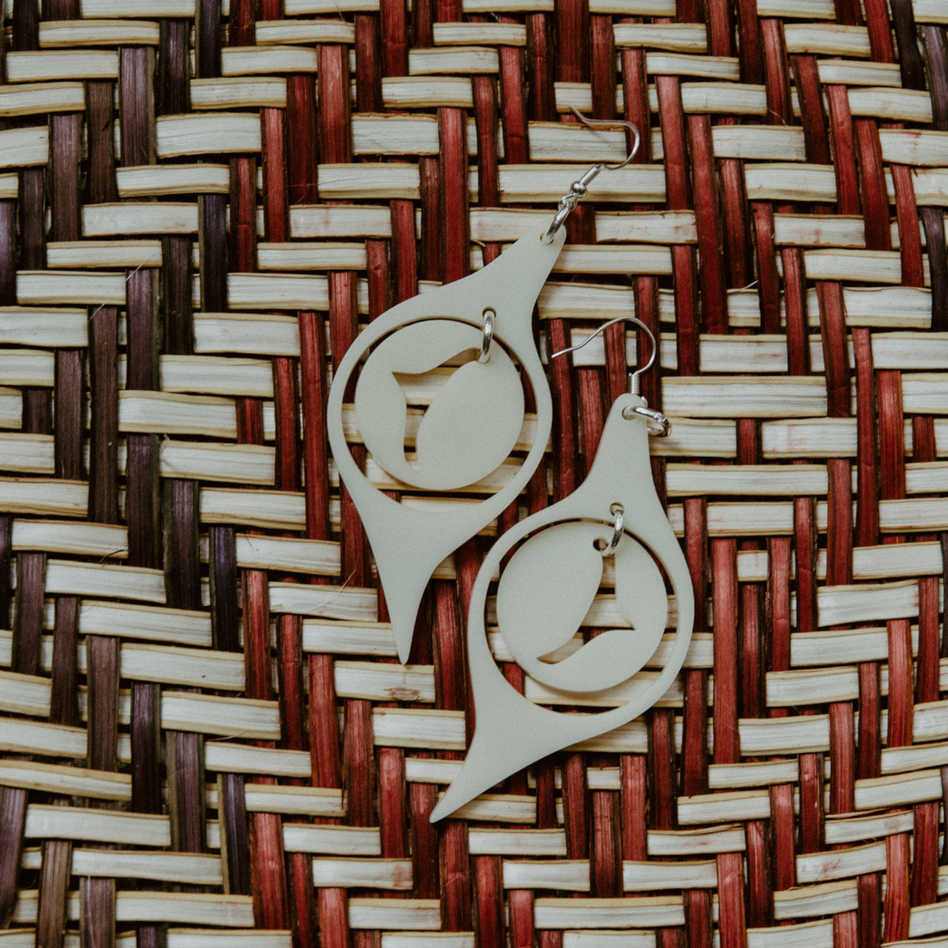 A pair of "Octopus Eye" earrings in ivory acrylic laying on a woven mat.