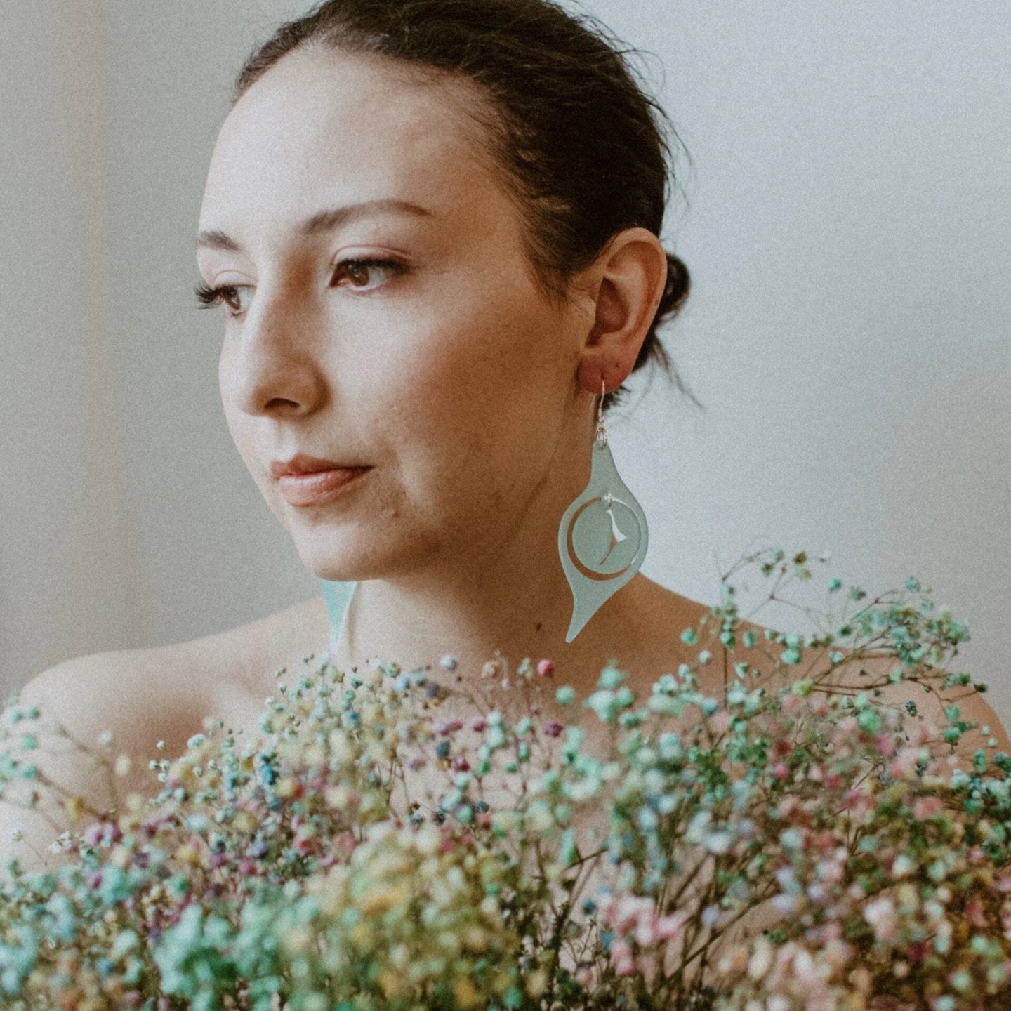 A model holding flowers wears the "Octopus Eye" earring from Copper Canoe Woman in seaglass color acrylic.