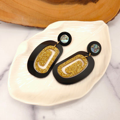 Pair of Copper Canoe Woman gold and black earrings on a white dish with a marble background.