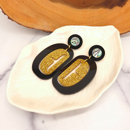 Gold and black acrylic earrings from Copper Canoe Woman on a white dish with a wooden background.