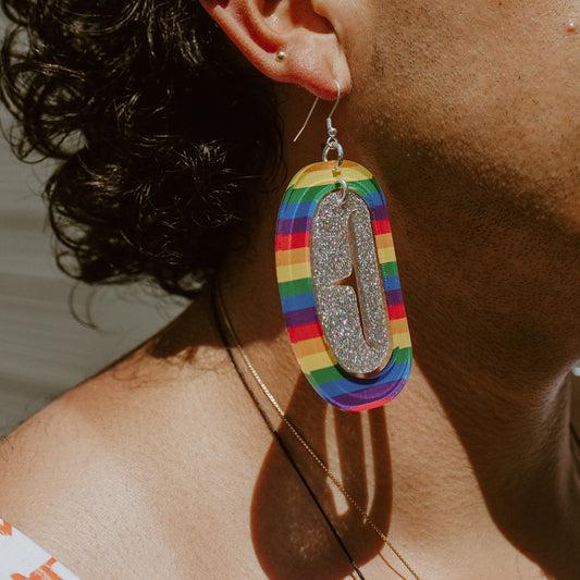 Closeup of a model wearing the large ovoid earring in rainbow and holographic glitter acrylic from Copper Canoe Woman.
