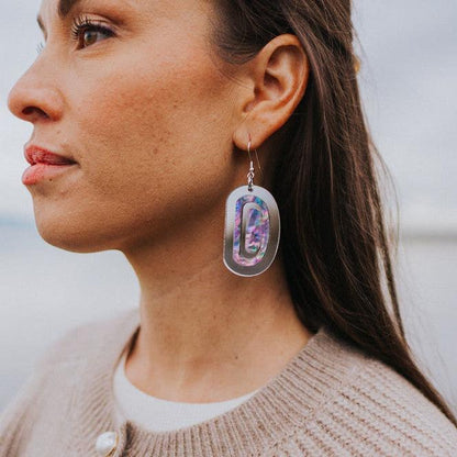 A woman by the beach wearing "Abalone Ovoid" earrings in silver mirror acrylic by Copper Canoe Woman.