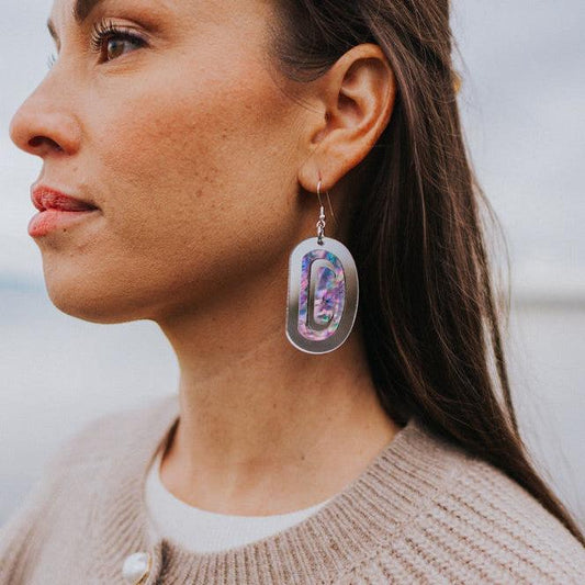 A woman by the beach wearing "Abalone Ovoid" earrings in silver mirror acrylic by Copper Canoe Woman.
