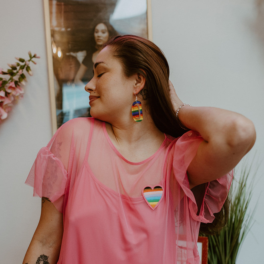 A model shows off the rainbow acrylic small ovoid earring with crescent cutout from Copper Canoe Woman.