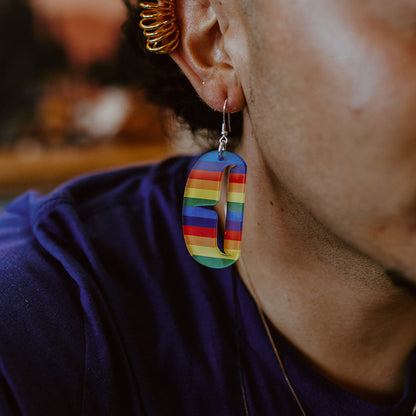 A close up of the Copper Canoe Woman small ovoid earring with trigon cutout in rainbow acrylic worn by a model.