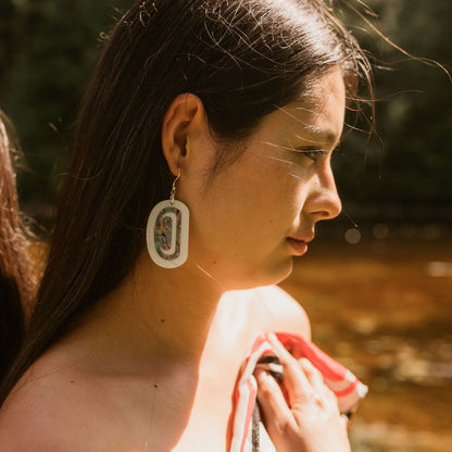 A woman in profile wears "Abalone Ovoid" earrings in white acrylic from Copper Canoe Woman.
