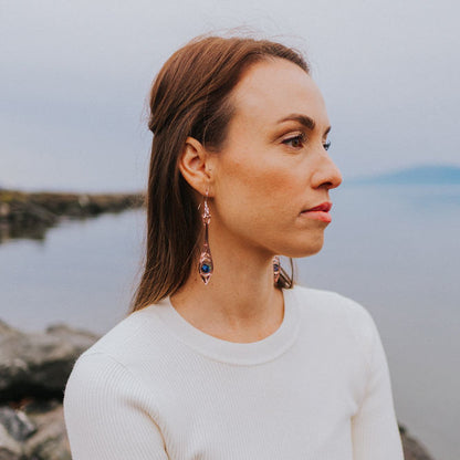 A woman at a beach wearing rose gold mirror acrylic "Paddle Song" earrings from Copper Canoe Woman.