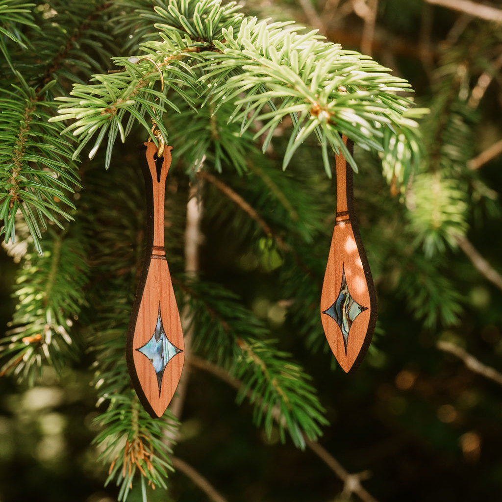 Cedar wood paddle-shaped earrings from Copper Canoe Woman hang from a pine branch.
