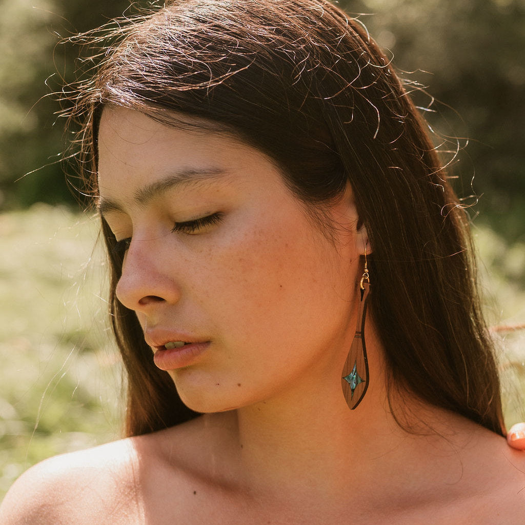 Model wearing cedar wood paddle shaped earring with star shaped abalone inlay from Copper Canoe Woman.