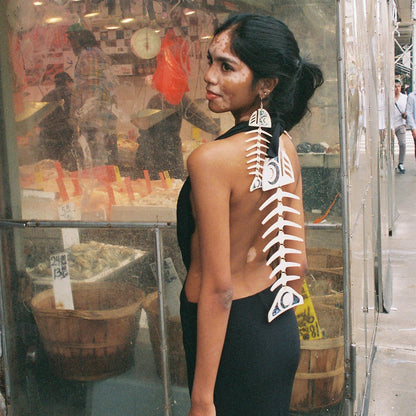 Person with an ivory copper canoe woman salmon ghost design on back of dress standing in front of a store window.