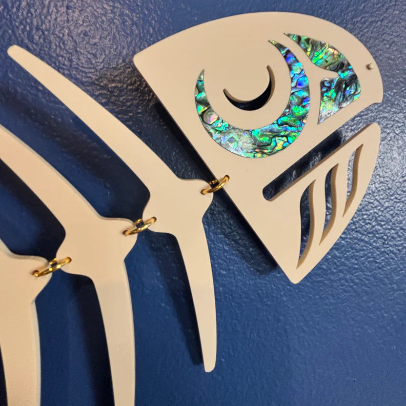 close up of ivory copper canoe woman salmon ghost design with abalone shell inlay on a blue background