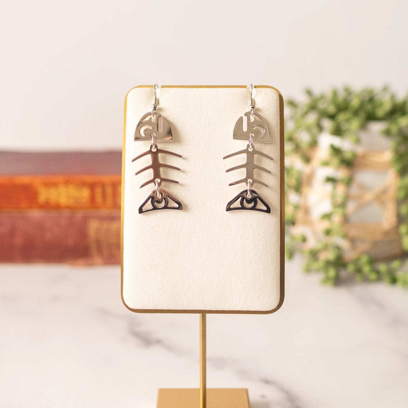 Copper Canoe Woman small salmon ghost earrings in white gold hanging from a jewelry display.