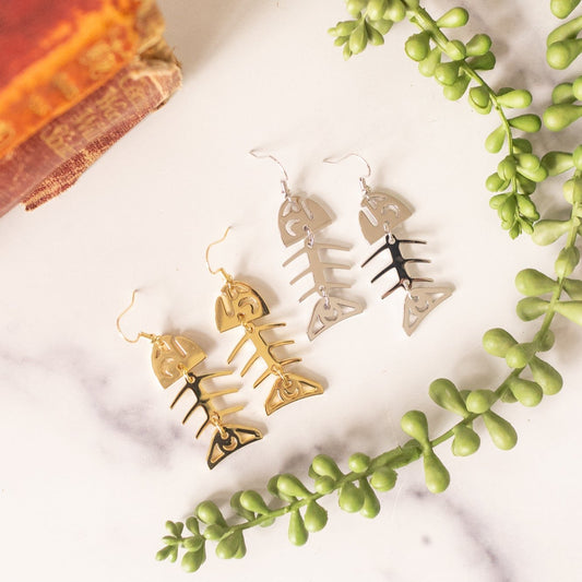 White and yellow gold small salmon ghost earrings from Copper Canoe Woman on a white marble tabletop.