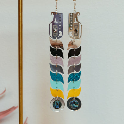 Blue and silver mirror acrylic serpent earrings hang from a display stand.