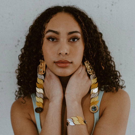 Model stares into the camera wearing yellow and gold mirror acrylic serpent earrings from Copper Canoe Woman.
