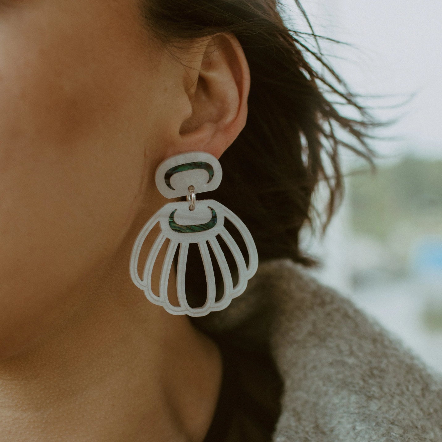 A close up of a model wearing pearl acrylic "Shell Woman" earrings from Copper Canoe Woman.
