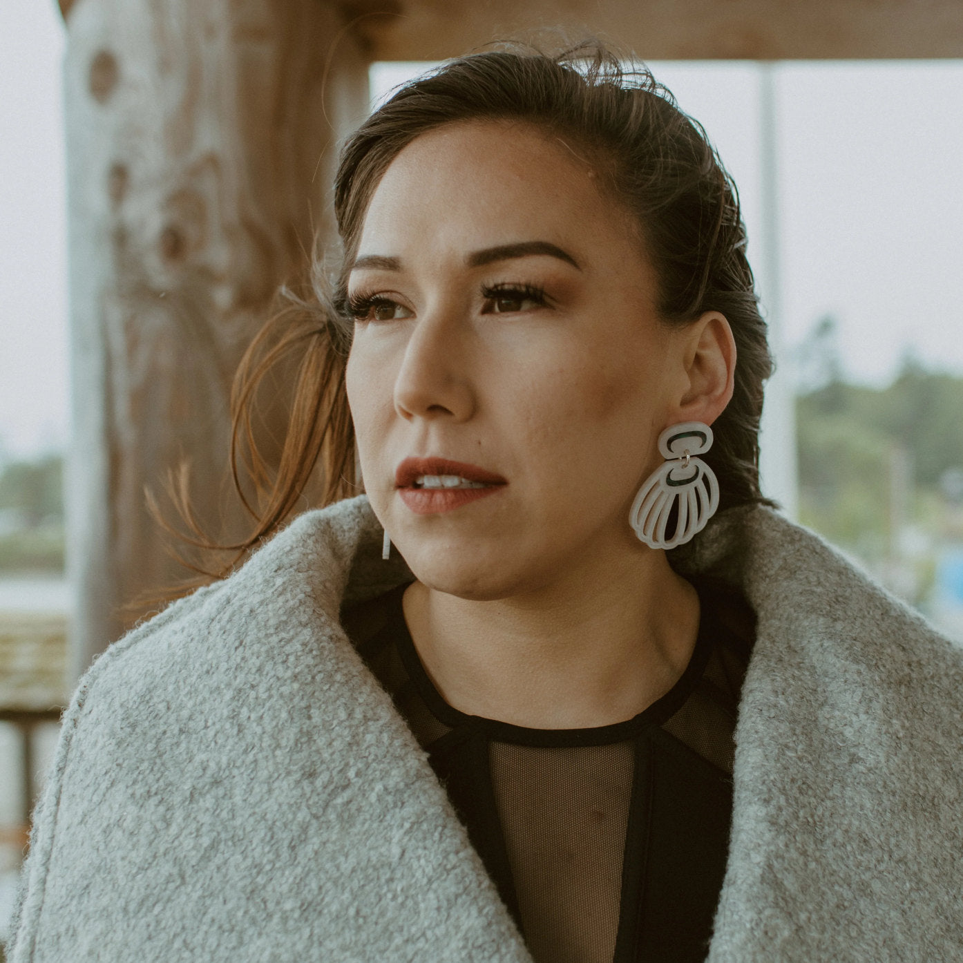 A model stares off camera wearing "Shell Woman" earrings in pearl acrylic from Copper Canoe Woman.