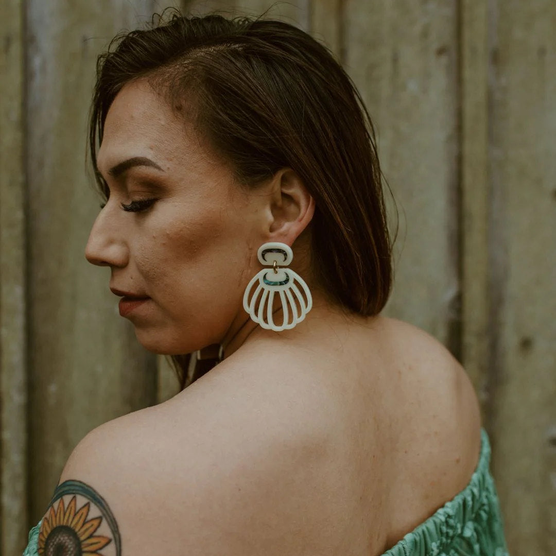 A model looks over her shoulder wearing an ivory acrylic "Shell Woman" earring from Copper Canoe Woman. 