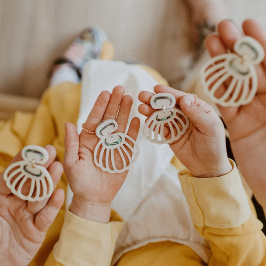 Hands hold pairs of Shell Woman earrings from Copper Canoe Woman in open palms.