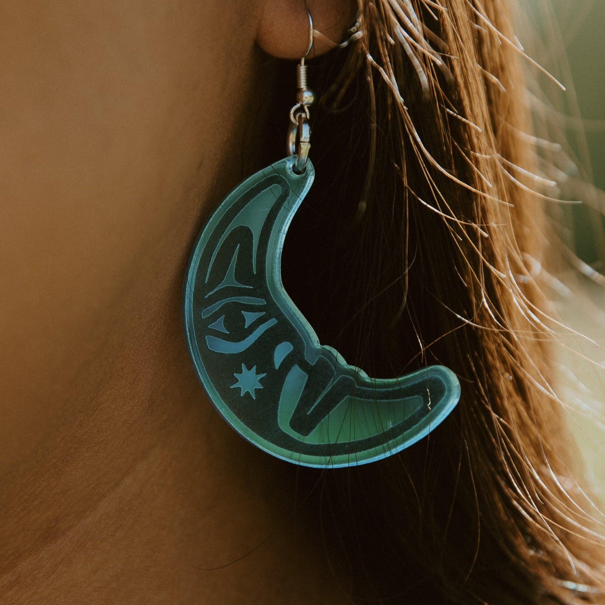 close up of woman wearing sky blue acrylic crescent moon engraved with formline art from copper canoe woman