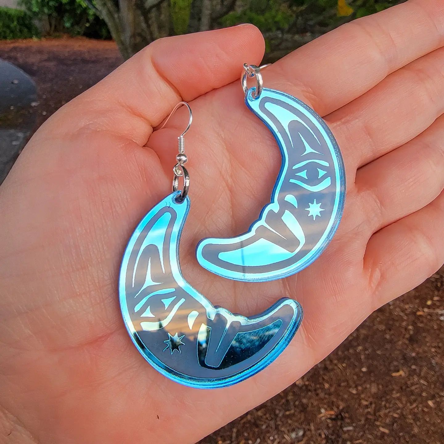 hand holding sky blue acrylic crescent moon engraved with formline art from copper canoe woman