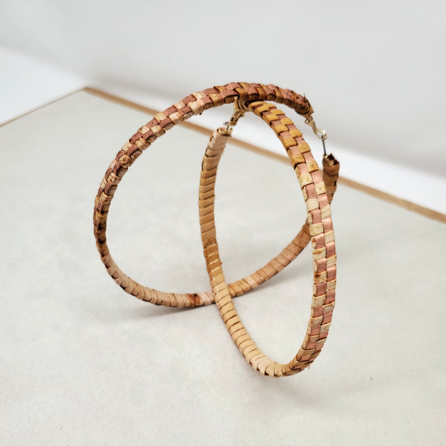 Pair of woven cedar hoop earrings with copper banding stand on a light gray surface