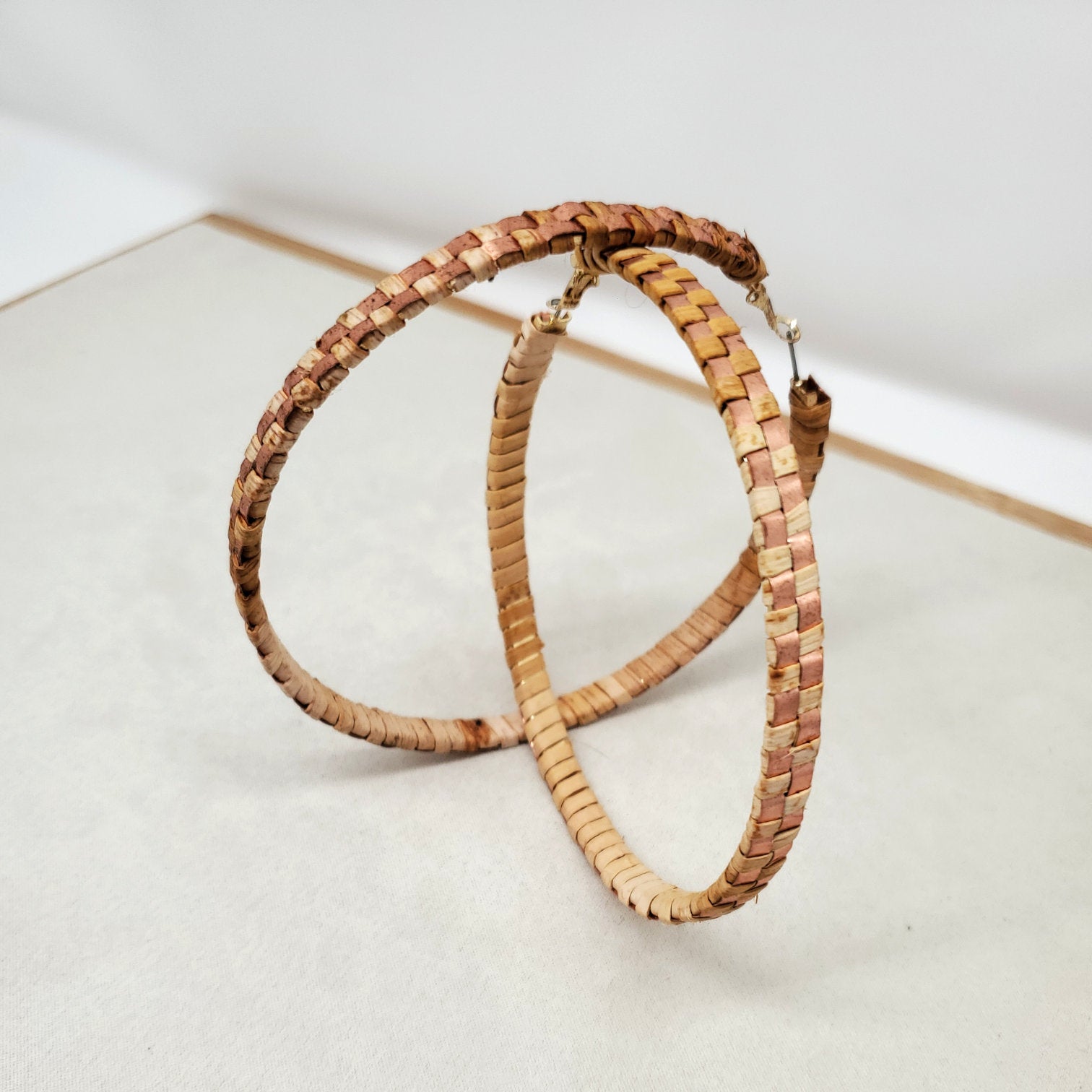 Pair of woven cedar hoop earrings with copper banding stand on a light gray surface