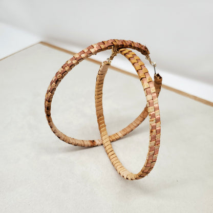 Pair of woven cedar hoop earrings with copper banding stand on a light gray surface