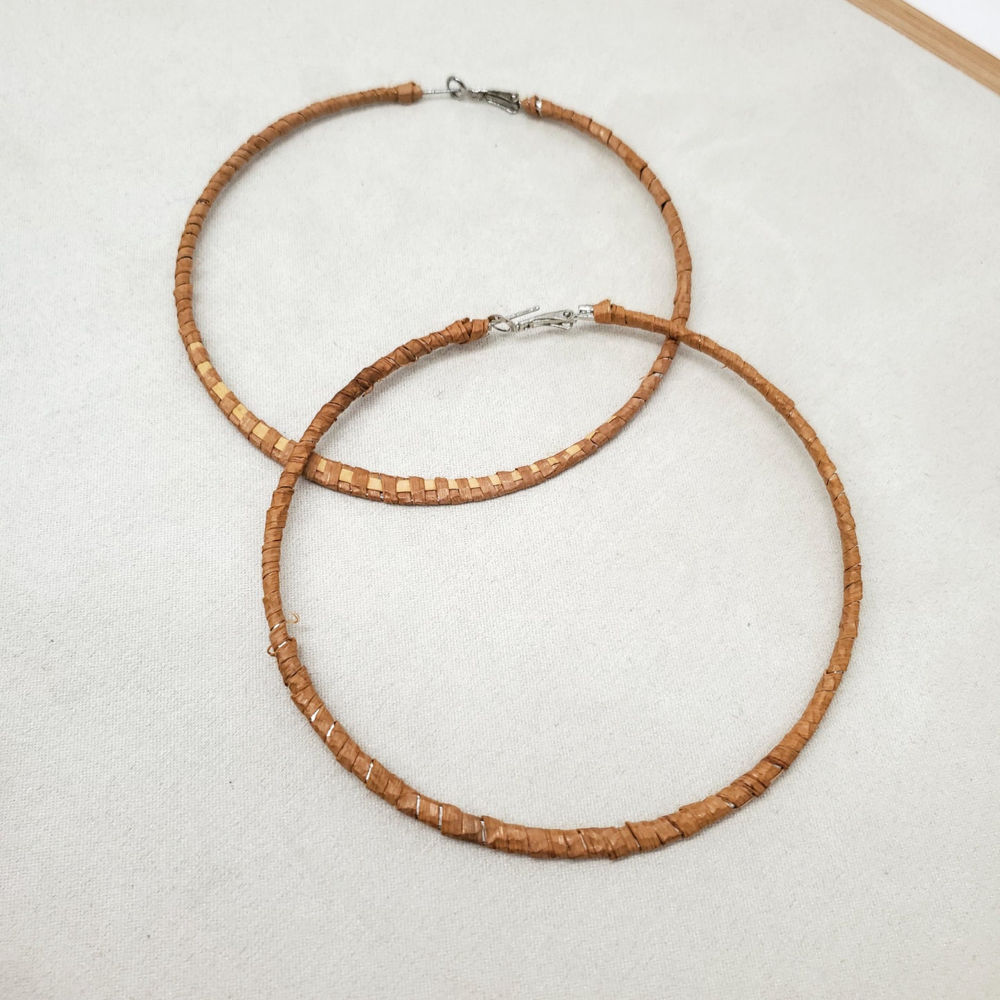 A pair of thin woven cedar hoop earrings on a light gray surface