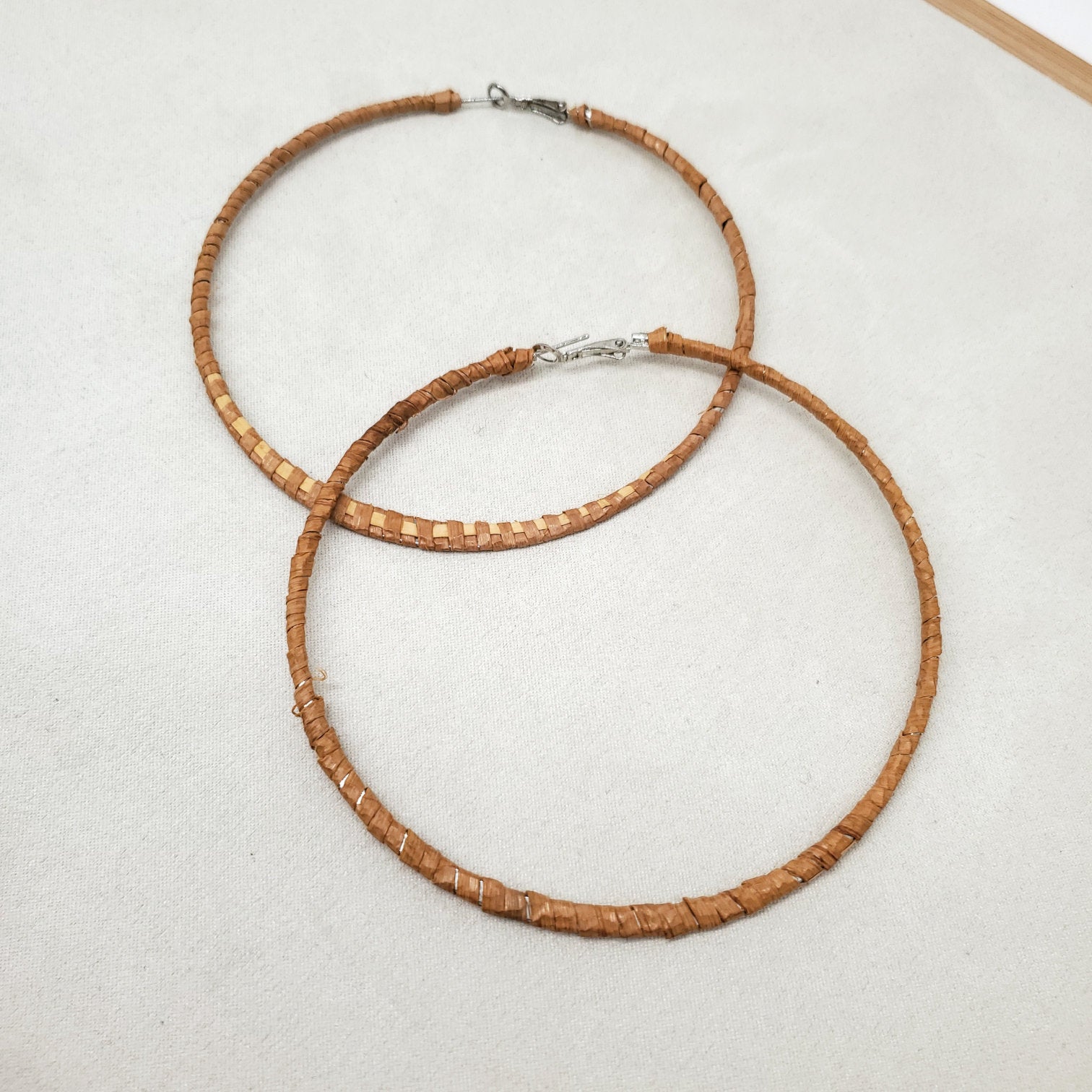 A pair of thin woven cedar hoop earrings on a light gray surface