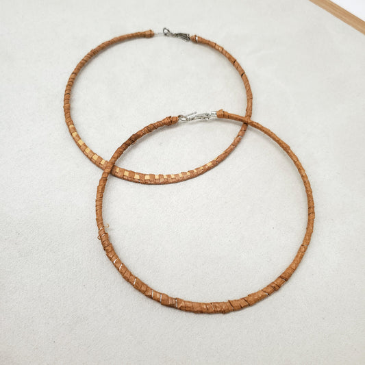 A pair of thin woven cedar hoop earrings on a light gray surface