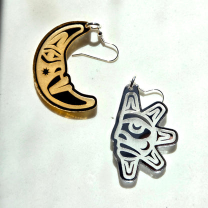 Two earrings, one sun-shaped and one moon-shaped with Coast Salish designs, on a white background from Copper Canoe Woman.
