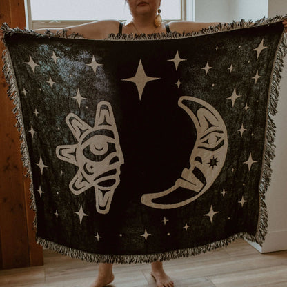 A figure holds open the back side of the "Hupal" sun and moon throw blanket from Copper Canoe Woman.