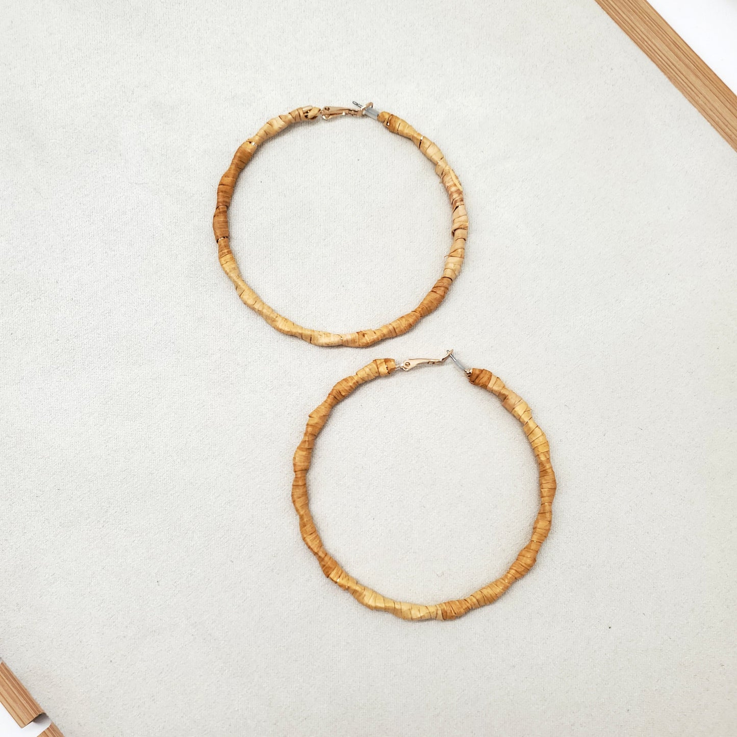 Two gold hoop earrings wrapped in cedar bark on a light gray surface.